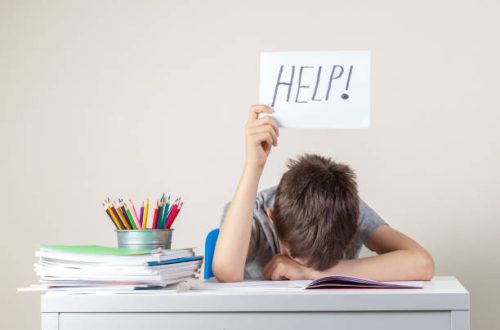 Sad tired frustrated boy sitting at the table with many books and holding help sign. Learning difficulties, education concept.