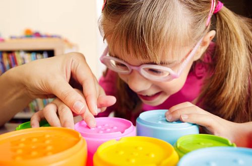 Little girl with poor vision is playing with colorful tactile toy cups as a part of occupational therapy with her teacher.